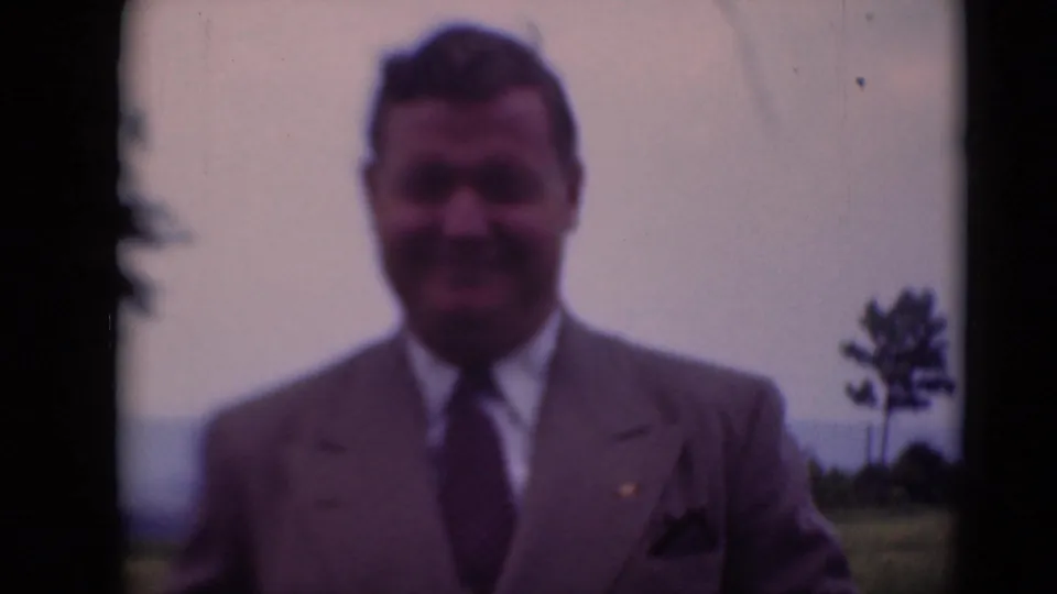 Adult man smiles toward the camera in 1948 Middletown, Pennsylvania, with rural background and soft 8mm texture.