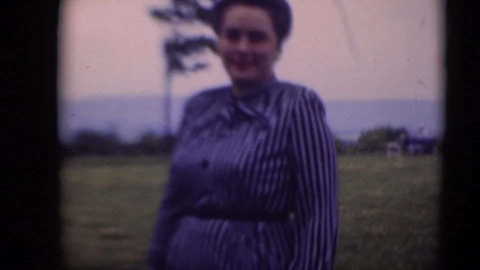 A woman in a striped dress smiles toward the camera in a Middletown, Pennsylvania field in late-1940s home-movie footage.
