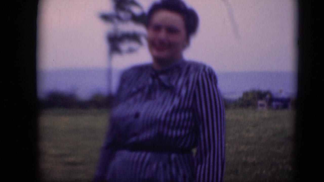 A woman in a belted striped dress stands outdoors in Middletown, Pennsylvania, with a distant tree and pale sky behind her.