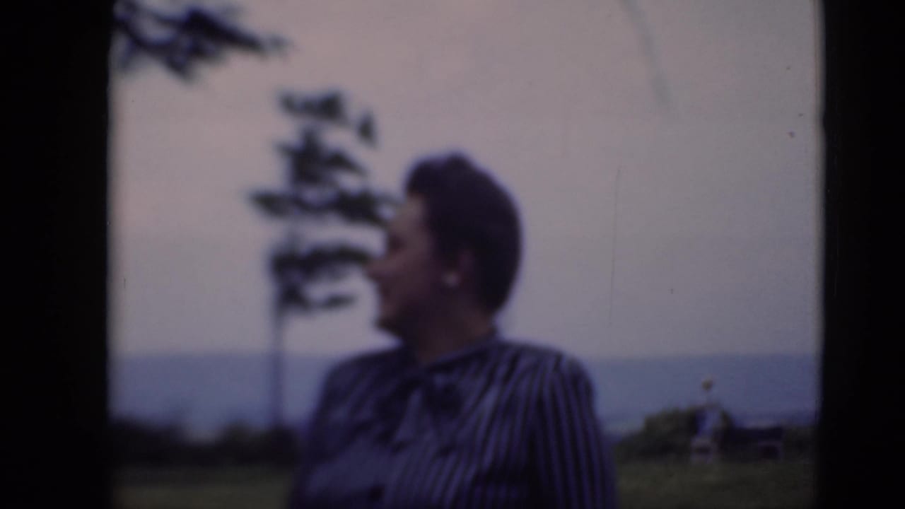 Woman in profile on a lawn, with trees and a distant horizon behind her.