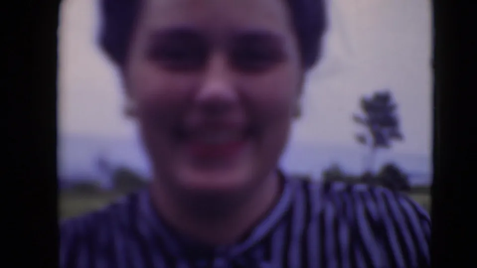 Close soft-focus 8mm view of the smiling woman in a striped blouse outdoors in Middletown, Pennsylvania, with lawn and sky behind her.
