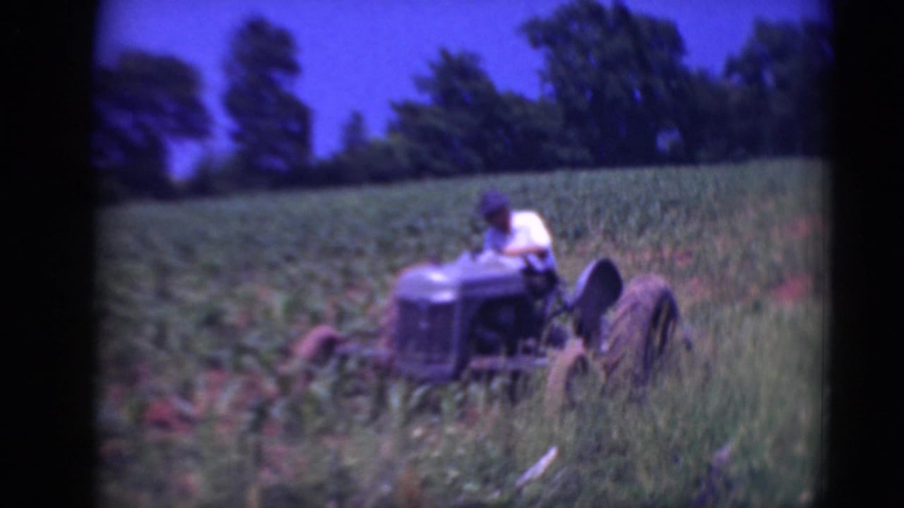 A man seated on an older tractor works through rows in a green Pennsylvania field, seen in soft 8mm color.