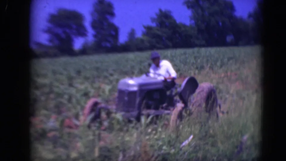 The driver and tractor appear closer to camera as the vehicle passes through crop rows in rural Middletown, Pennsylvania footage.