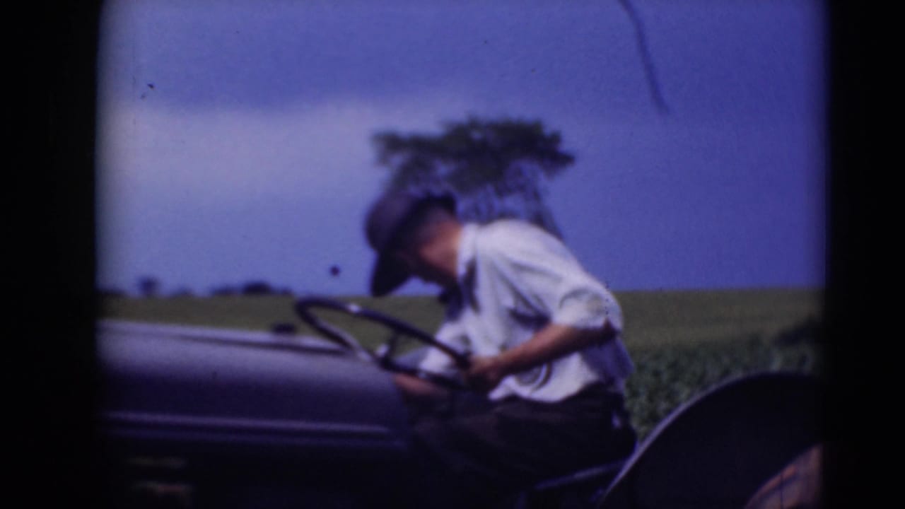 Man in a hat leans over the steering wheel of a tractor in a field.