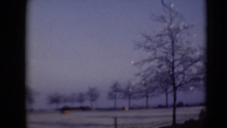 Winter home-movie frame showing bare trees across a snowy Middletown landscape, with distant structures or landforms softened by focus.
