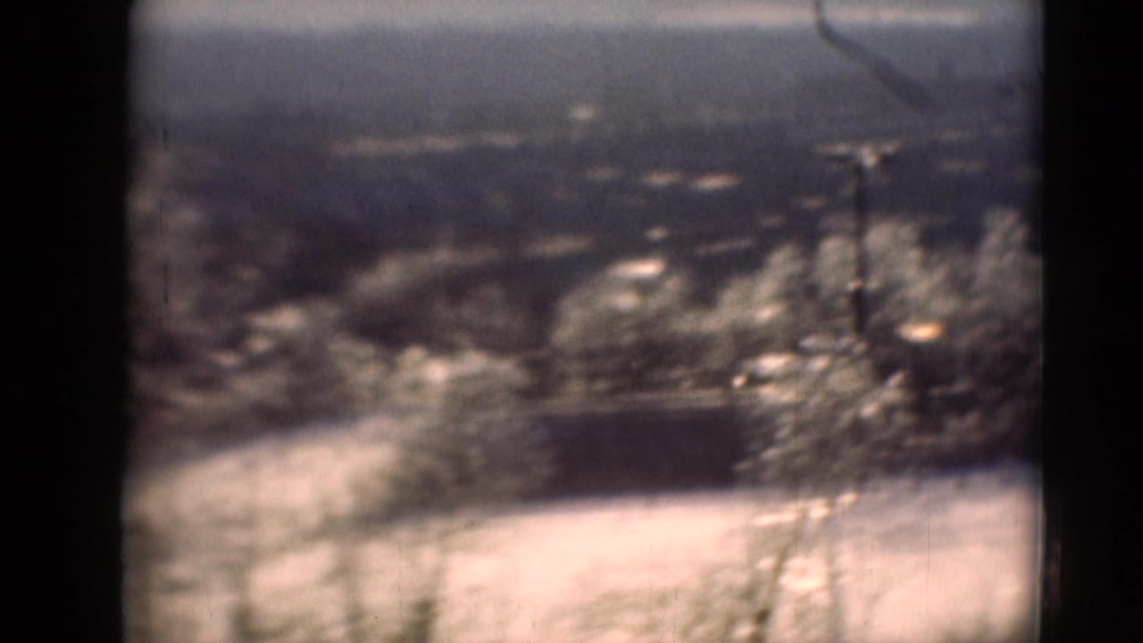 Soft 8mm frame from Middletown, Pennsylvania, with pale ground, trees, a low dark structure, and distant hills.