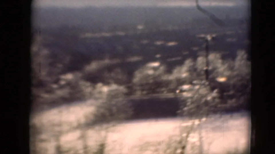 Soft 8mm frame from Middletown, Pennsylvania, with pale ground, trees, a low dark structure, and distant hills.