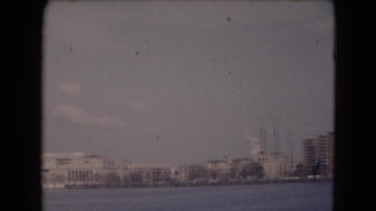 Reported Middletown, Pennsylvania shoreline with low buildings, smokestacks, bare trees, water, and soft 8mm exposure.