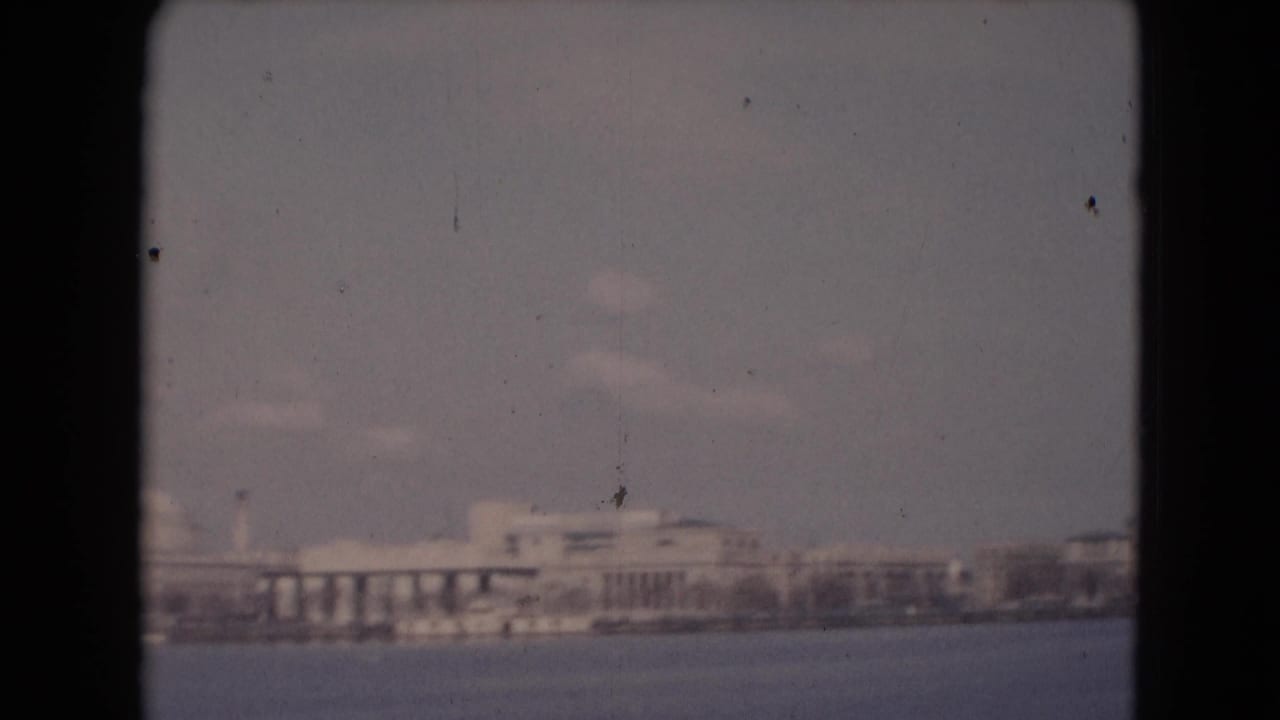Reported Middletown waterfront view with a broad low building, column-like bays, distant shoreline, haze, and visible 8mm wear.