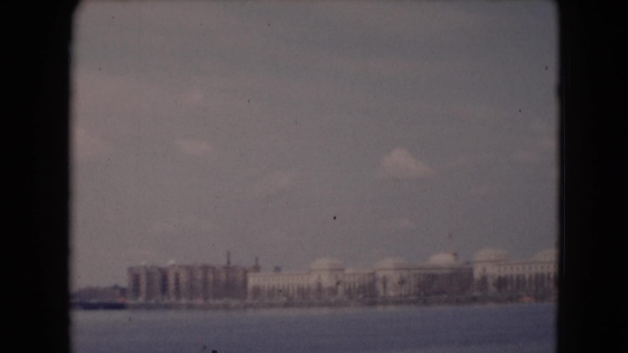 1948 8mm frame of a distant Pennsylvania waterfront, showing low structures, domed buildings, and open water in the foreground.