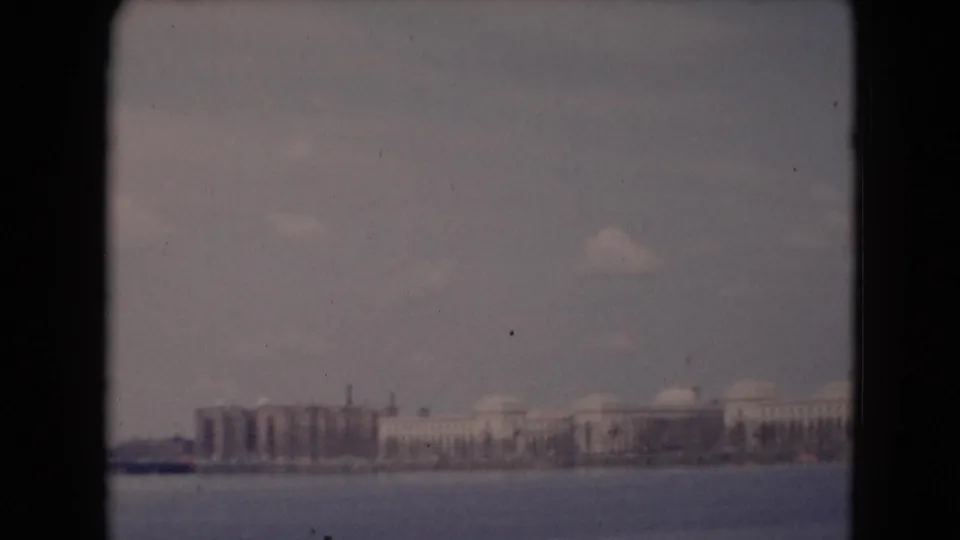 1948 8mm frame of a distant Pennsylvania waterfront, showing low structures, domed buildings, and open water in the foreground.
