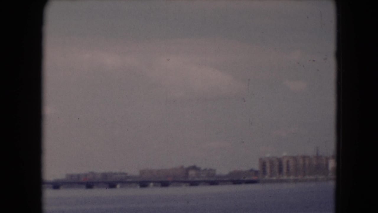 Distant long bridge over a wide river with far-shore buildings under a hazy sky.
