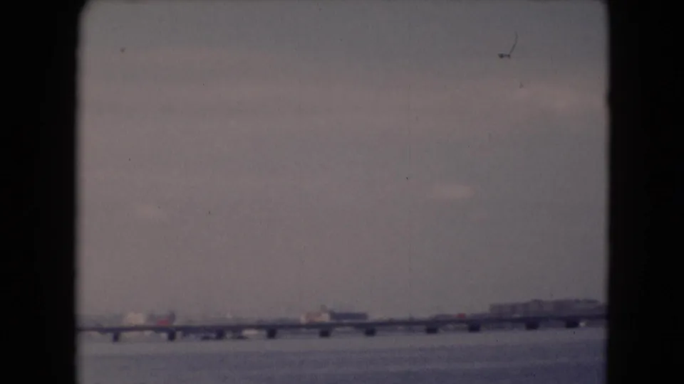 Soft 8mm frame of a long river bridge near Middletown, Pennsylvania, with small far-shore structures and muted overcast light.