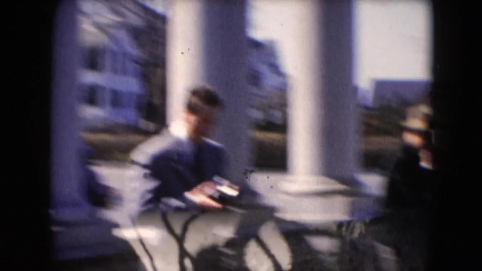 In Middletown, Pennsylvania home-movie footage, a suited man stands outside near white columns with a small camera in his hands.