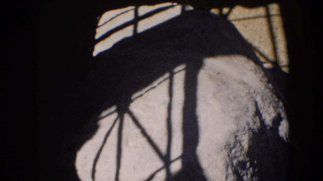 The footage cuts closer to a pale textured surface crossed by dark rail or window shadows, with heavy 8mm grain and edge darkness.