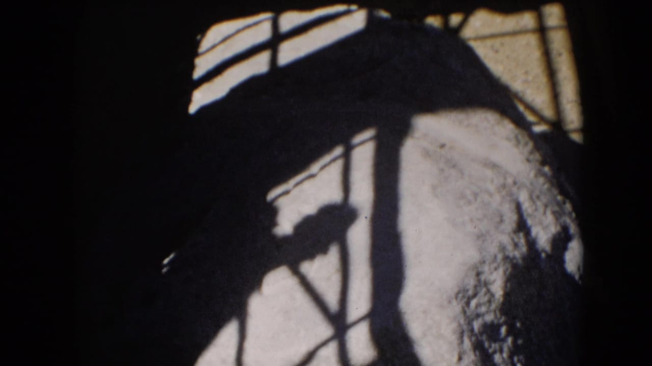A dark human-like shadow shape briefly appears within angular shadow lines on a pale exterior surface in the 8mm footage.
