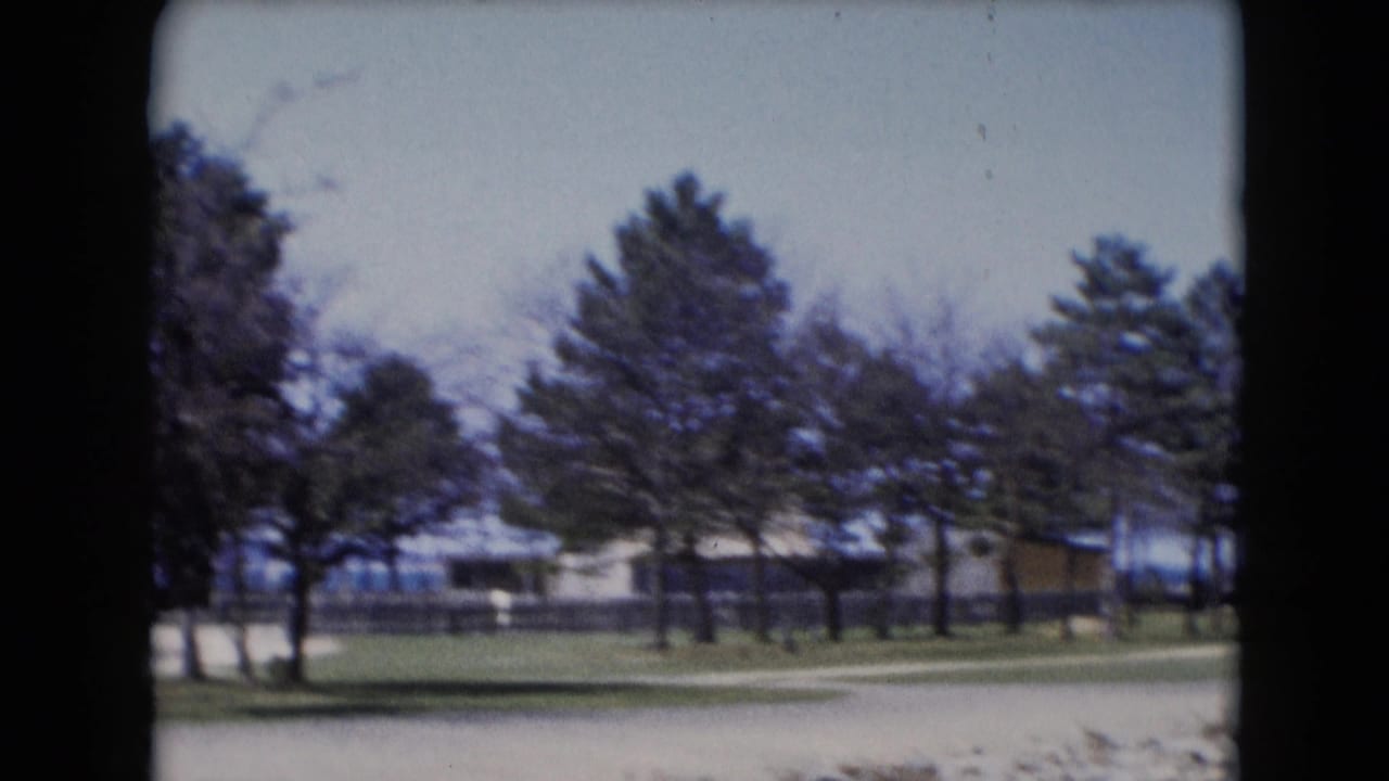 1940s 8mm view in Middletown, Pennsylvania, showing trees, grass, low buildings, and a pale road near the water.