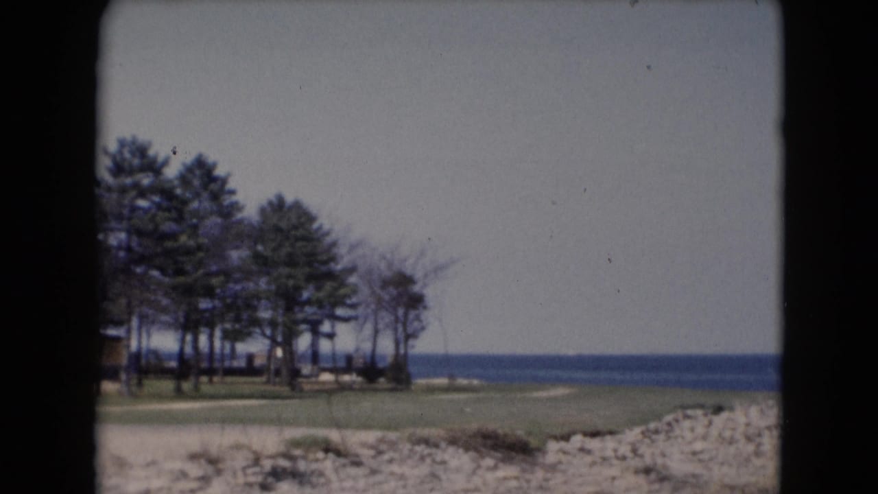 Handheld 8mm frame showing a tree cluster, open grass, rocky edge, and broad water at a Middletown shoreline.