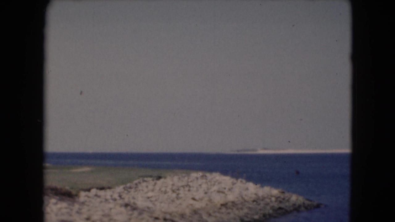 Blue sea and pale sky with a rocky shoreline framed by dark 8mm film edges.