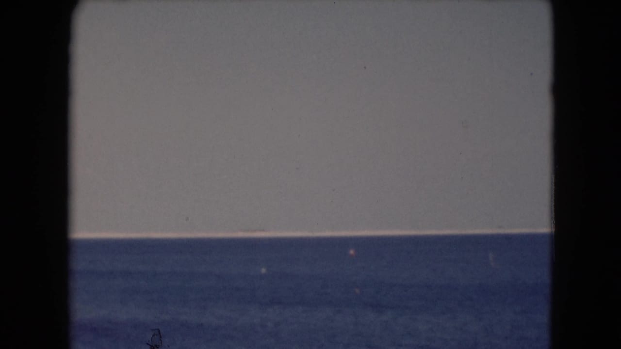 Open blue water and pale sky divided by a low horizon within dark film borders.
