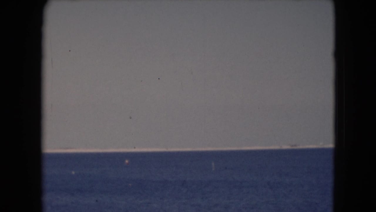 1940s 8mm frame of calm blue water under a pale sky, with visible contact-sheet borders and light film wear.