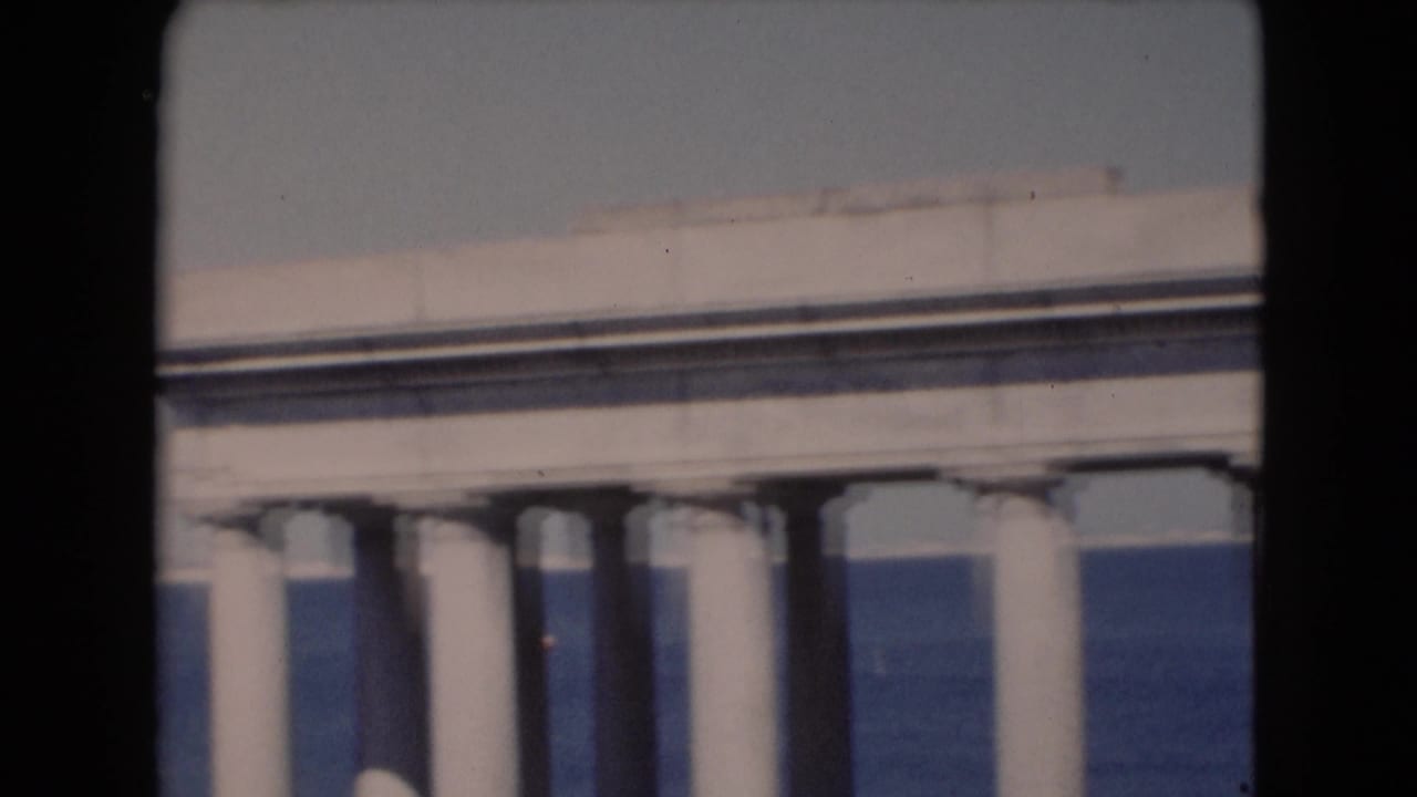 Soft 8mm view of a white colonnade and roofline, with blue water visible beyond the structure.
