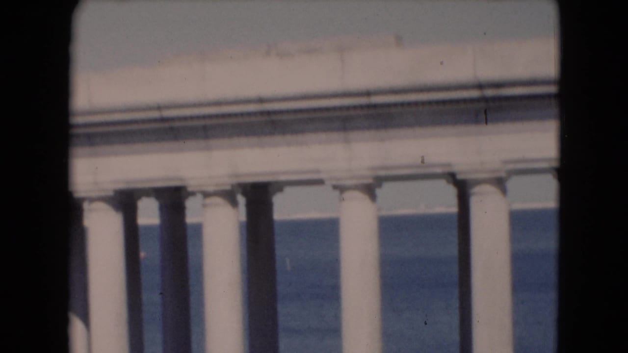 A later frame shows a pale roofline above white columns, with blue water behind and a dark 8mm frame edge at the side.