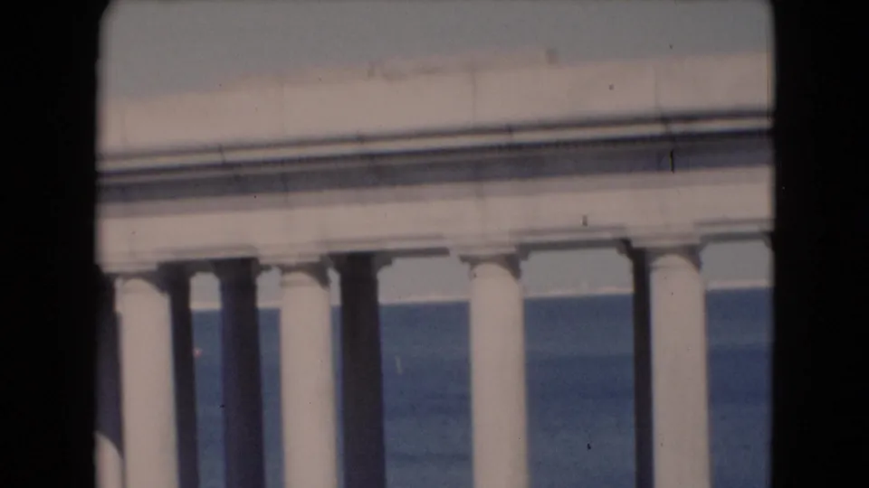 A later frame shows a pale roofline above white columns, with blue water behind and a dark 8mm frame edge at the side.