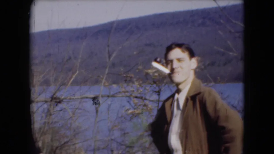 In Middletown, Pennsylvania home-movie footage from 1948, a man in a brown jacket stands smoking beside a lake and distant hills.