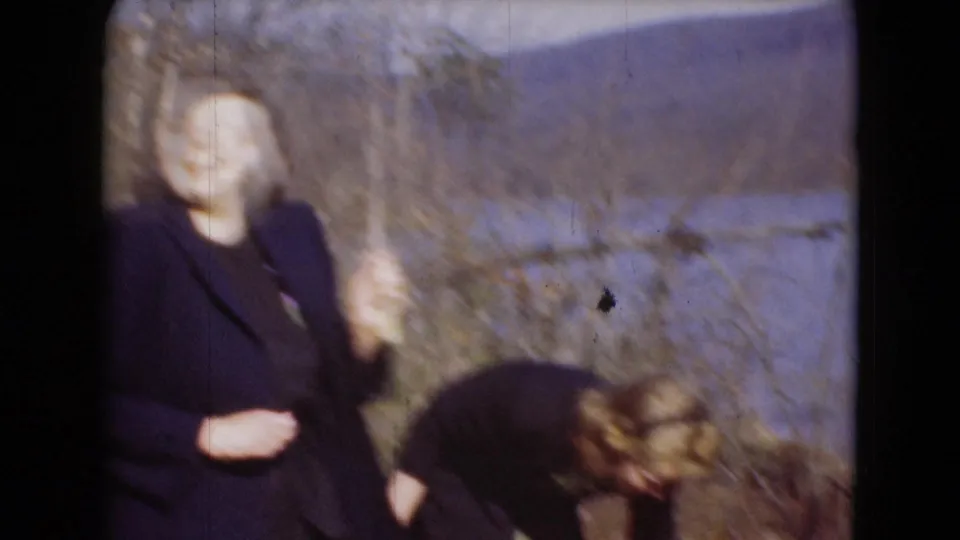 A woman gestures toward the camera while another bends down in soft, motion-blurred 1948 lakeside home-movie footage from Middletown.