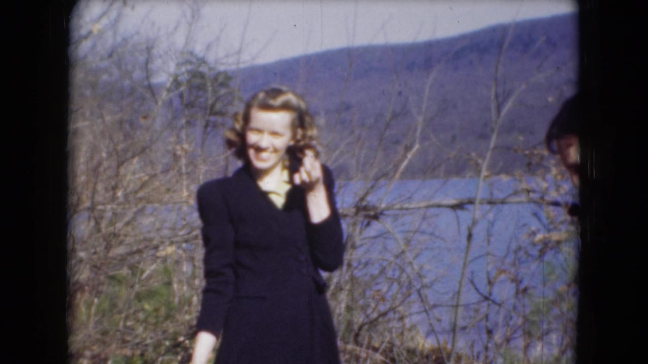 A smiling woman in a dark suit touches her hair near the lake in 1948 Middletown, Pennsylvania home-movie footage.