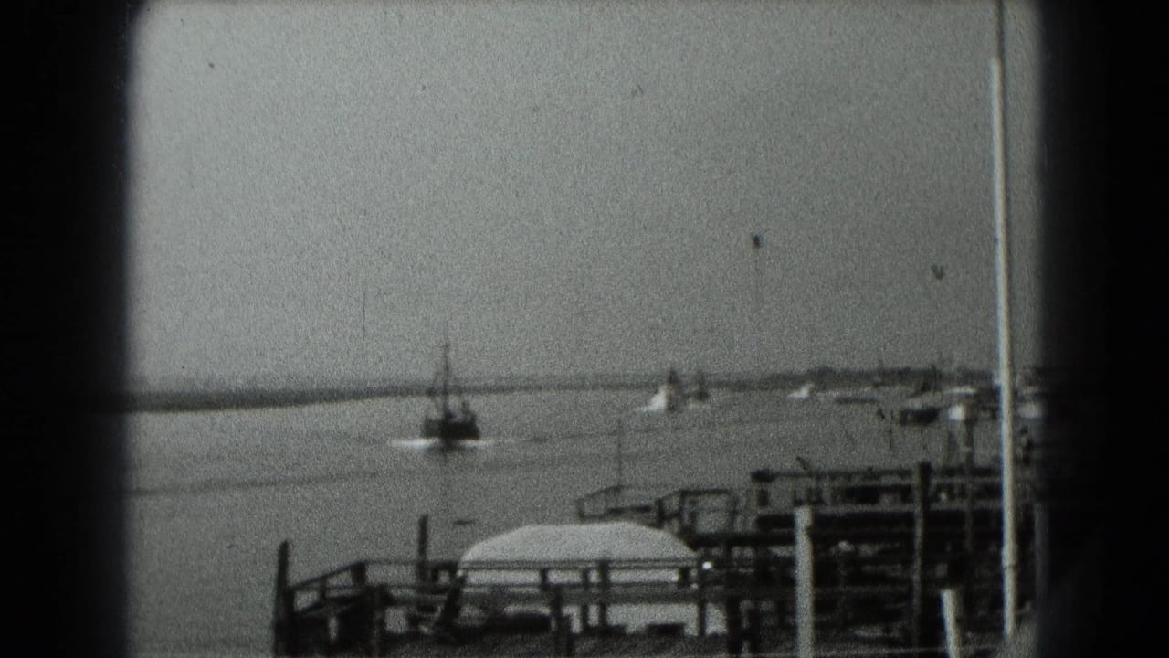 Black-and-white 8mm frame of a small boat moving across calm water near dock railings in archival Middletown, Pennsylvania footage.