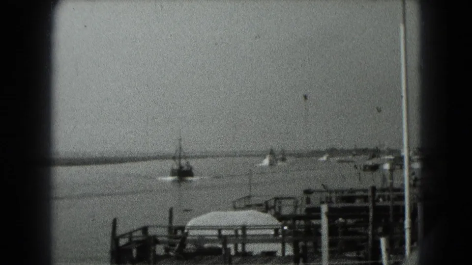 Black-and-white 8mm frame of a small boat moving across calm water near dock railings in archival Middletown, Pennsylvania footage.