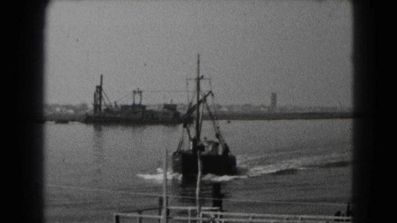 Black-and-white archival frame showing a small working boat or fishing boat passing dock structures with a distant shoreline behind it.