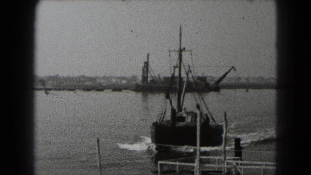 Small boat moves across harbor water with a larger industrial vessel in the distance.