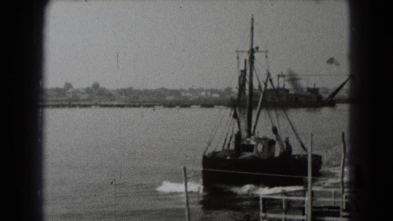 The small harbor boat continues past the camera in black-and-white 8mm footage, with a larger industrial vessel and shoreline behind it.