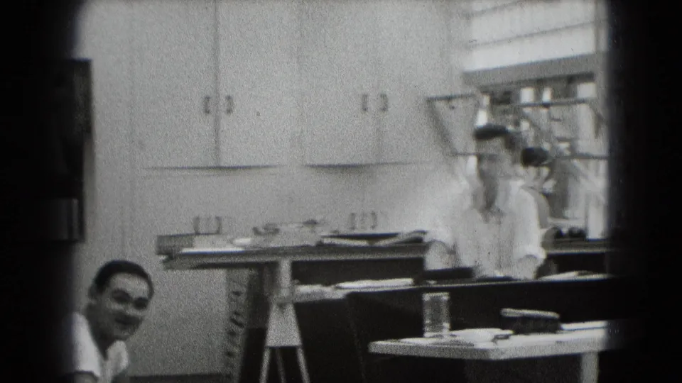 1948 home-movie frame from Middletown, Pennsylvania, showing two adult men in a modest interior with cabinets and a cluttered table.