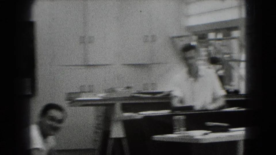A 1948 Middletown interior frame shows a man by a cluttered table, with another smiling man partly visible in the foreground.