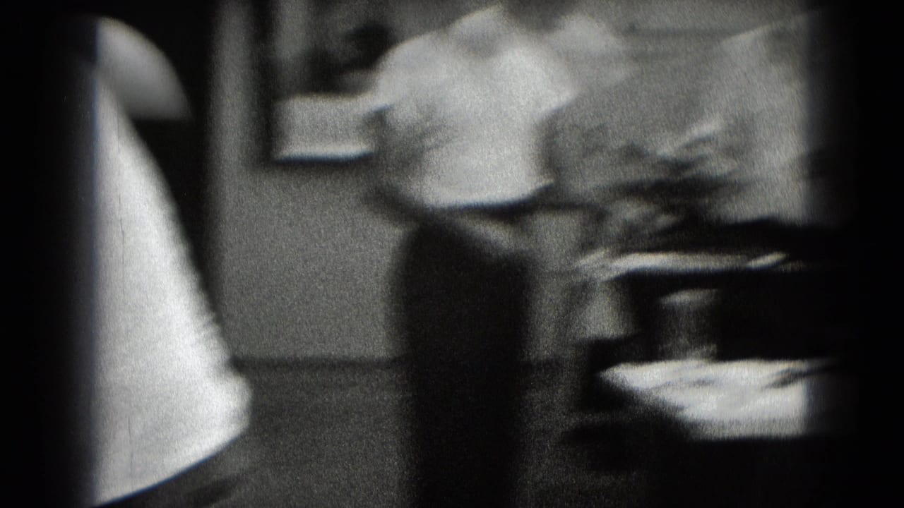 Soft, blurred workshop interior with a man moving near a table and dark film edges.