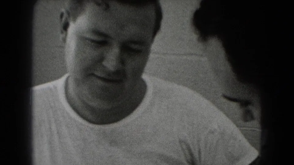 End frame from Middletown archival footage showing one man looking down at the work surface as another is partly seen beside him.