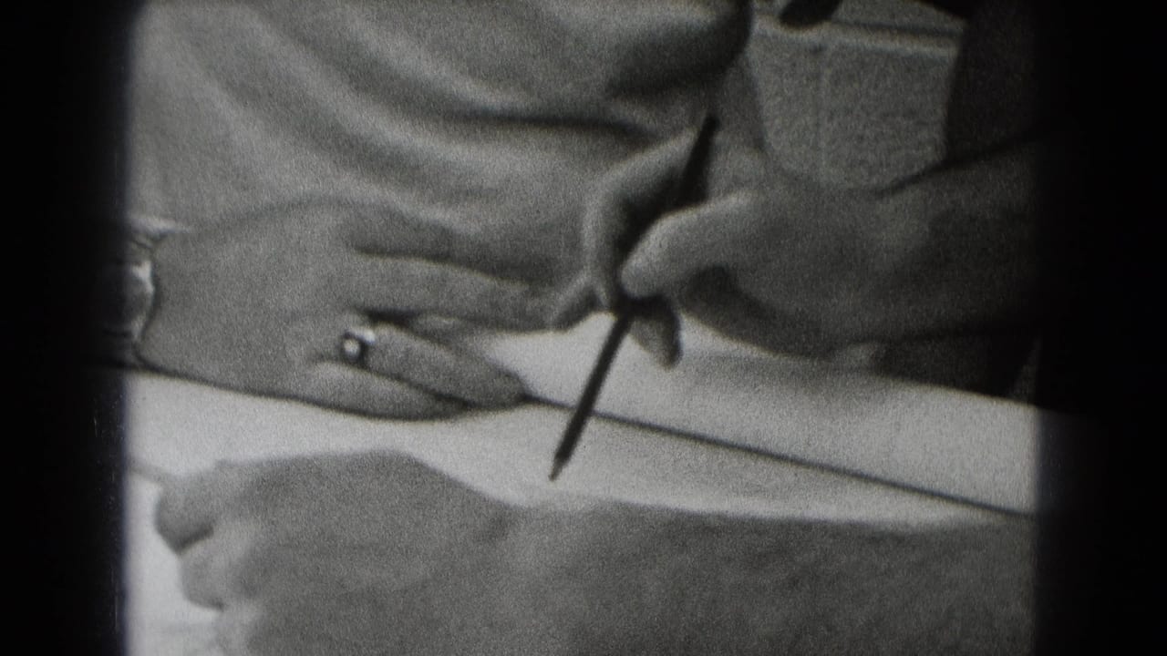 Hands hold a pencil over paper while another hand with a ring rests nearby.