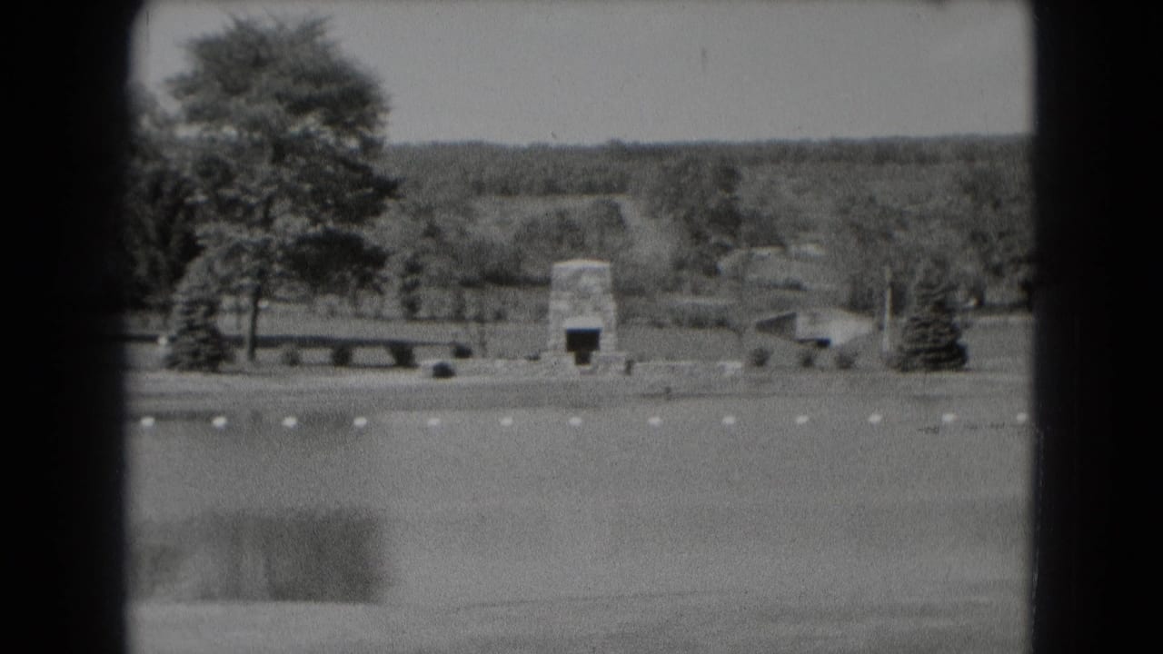 Black-and-white park view with pond, stone marker, trees, bench, and distant hills.