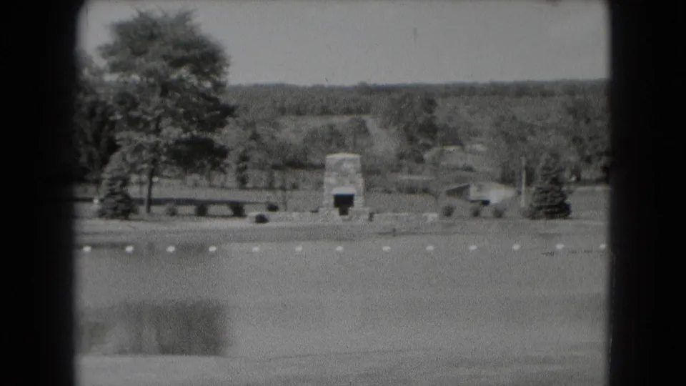 1975 Middletown, Pennsylvania park footage showing a pond foreground, stone marker, bench, trees, and distant wooded hills.
