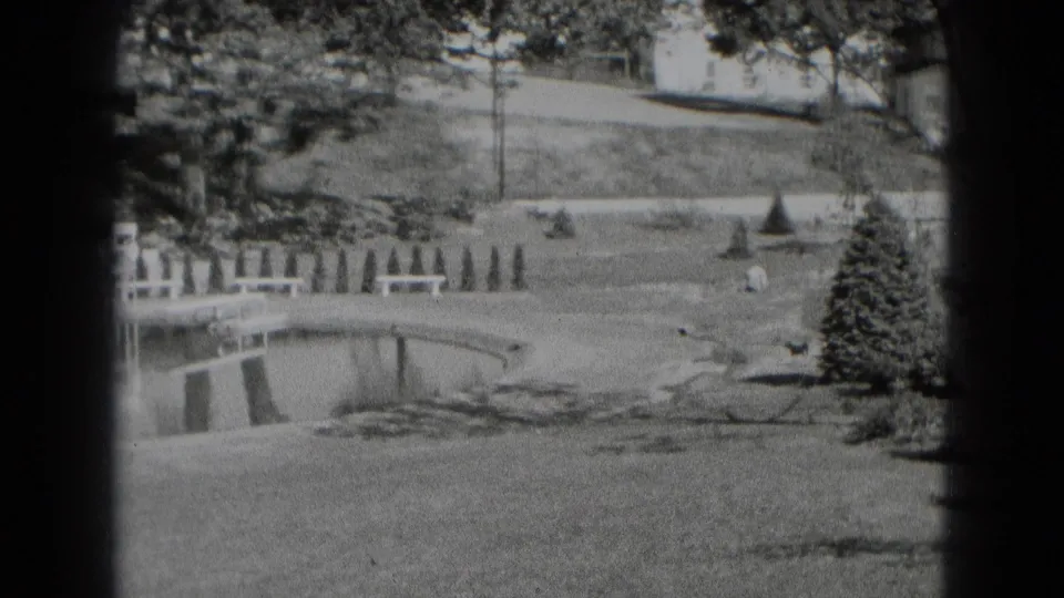 1975 Middletown, Pennsylvania 8mm frame showing a calm creek or pond edge bordered by grass, benches, trees, and a low crossing.