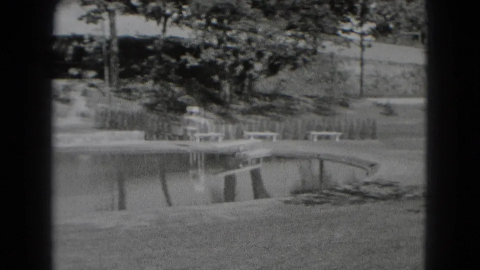 Black-and-white 8mm view of a landscaped creek edge in Middletown, Pennsylvania, with benches, trees, shrubs, and a curved shoreline.