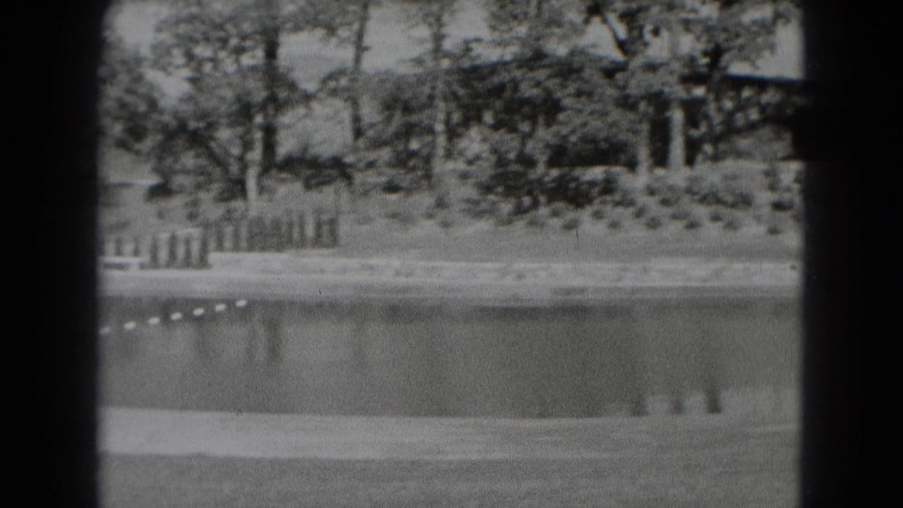 Roped water area beside grass, trees, and fencing in a park setting.