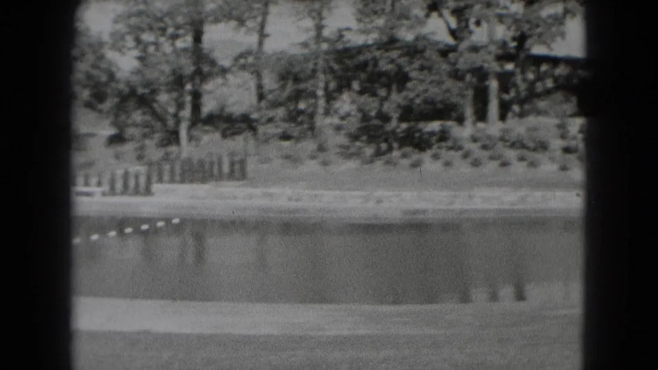 1975 Middletown, Pennsylvania home-movie frame showing a roped lagoon or pool with trees, fence sections, lawn, and distant hillside.