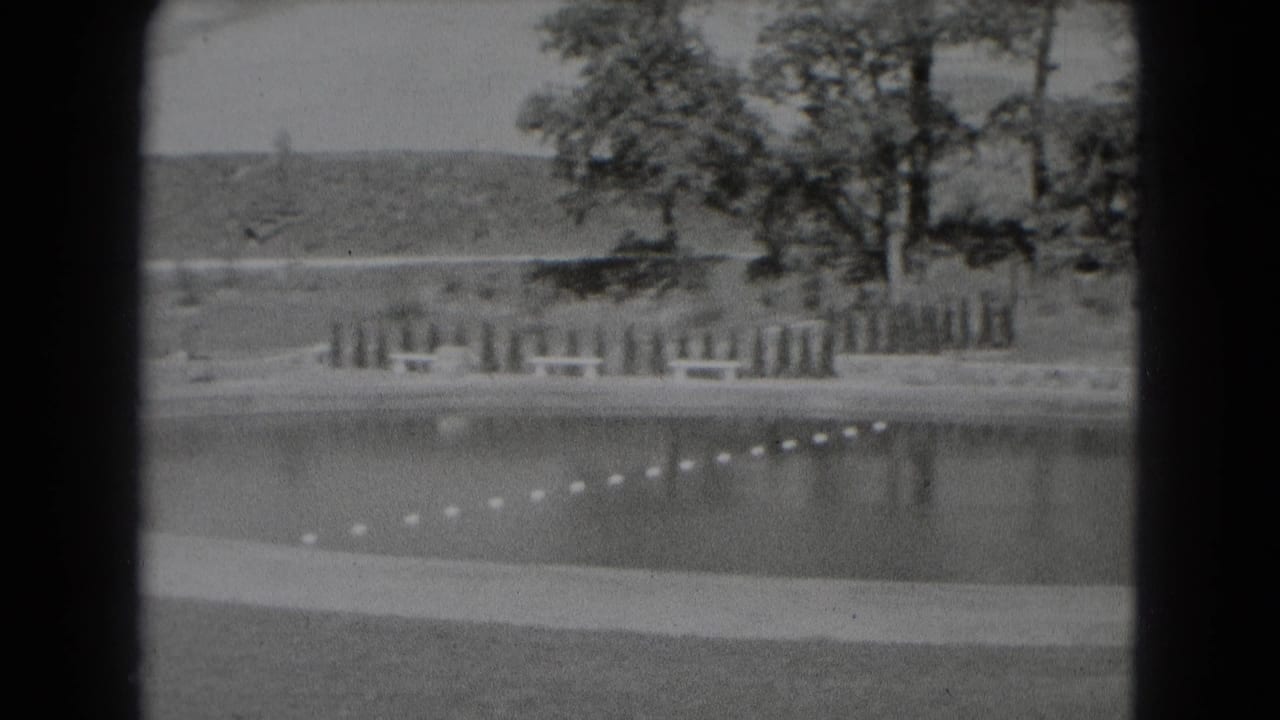 Lagoon edge with rope floats, trees, fence sections, and a distant hillside.