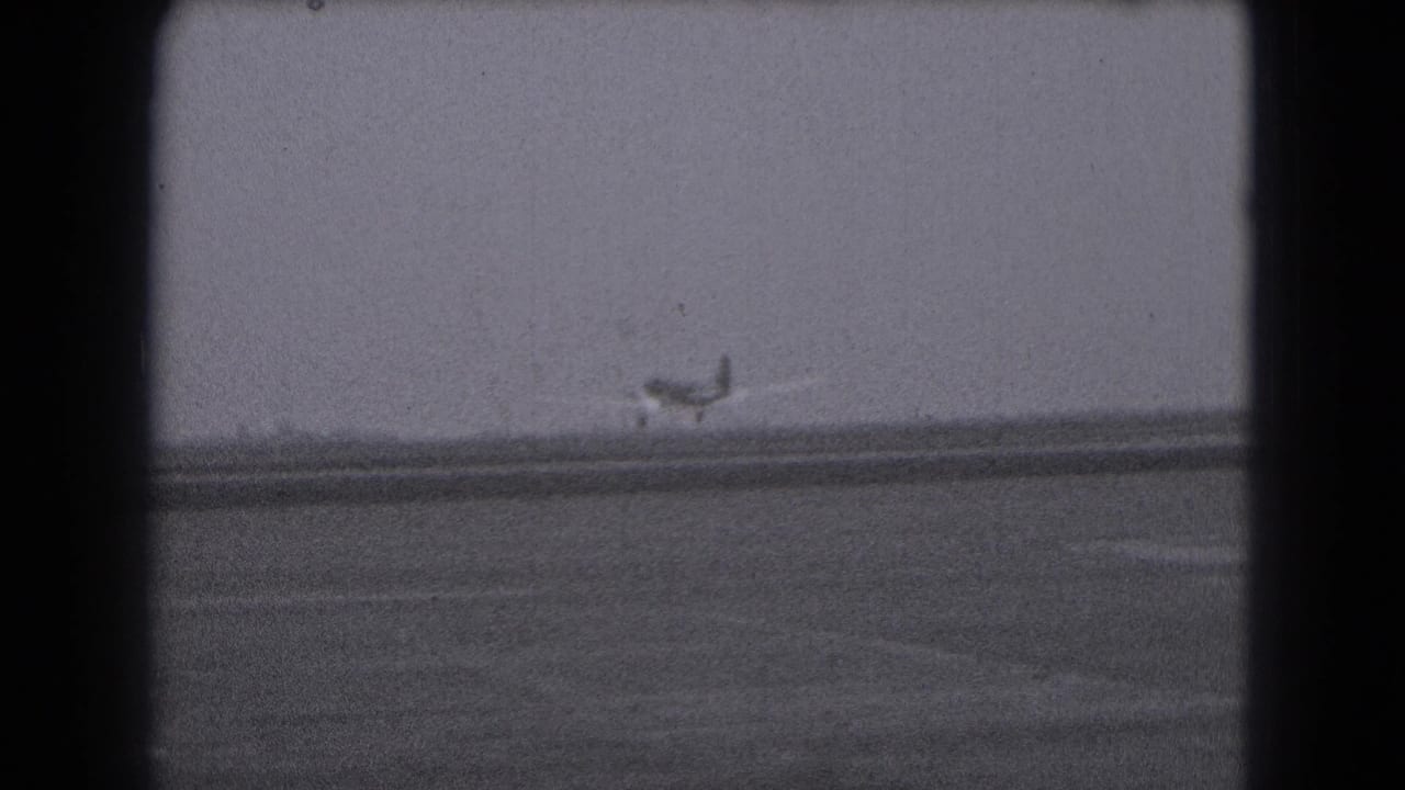 Distant propeller airplane on a runway, viewed through 1975 8mm home-movie framing in Middletown, Pennsylvania.