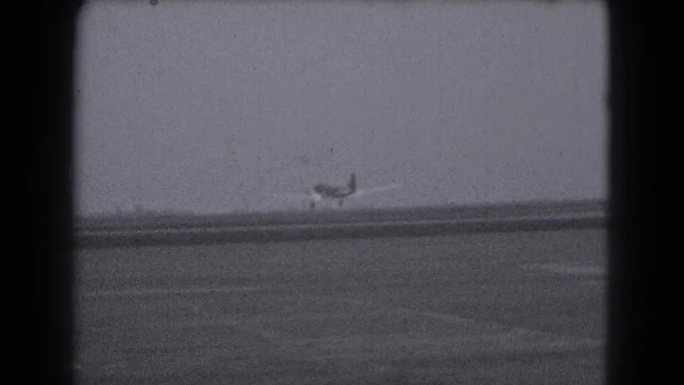 Distant propeller airplane on a runway, viewed through 1975 8mm home-movie framing in Middletown, Pennsylvania.